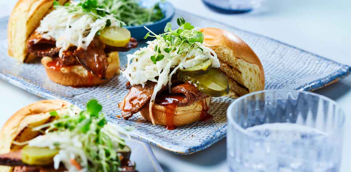BBQ brisket sliders topped with creamy coleslaw and microgreens on a blue plate.