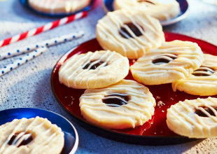 Round thumbprint-style cookies with blueberry pie filling sitting on a bright yellow plate.