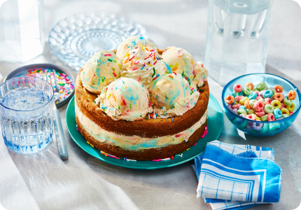 aqua cake plate with chocolate chip cookie birthday cake ice cream cake with scoops of ice cream and whipped cream on top, and a side bowl of fruit hoops cereal