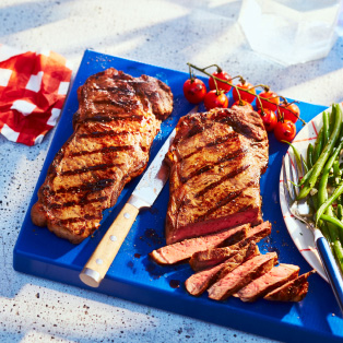 Marble surface with blue cutting board topped with platter of Sterling Silver Striploin Grilling Steak