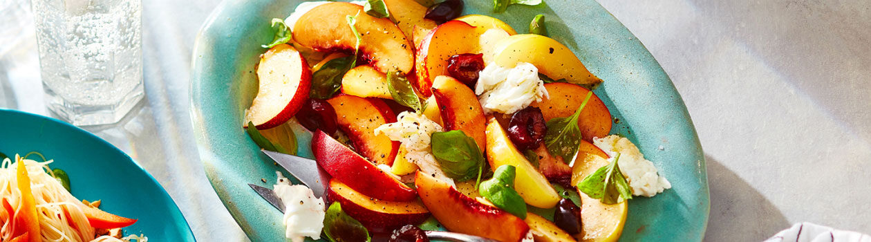 Light green serving platter topped with a Stone Fruit Caprese Salad with serving spoons.