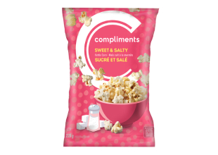A pink packet of Compliments Sweet & Salty Kettle Corn, featuring an illustration of a salt shaker and sugar cubes on the front of the pack, along with a pink bowl of the popcorn.