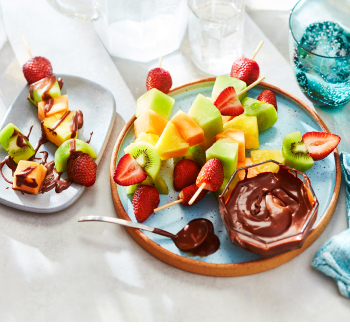 plate of fruit skewers with a bowl of chocolate sauce for dipping on the side