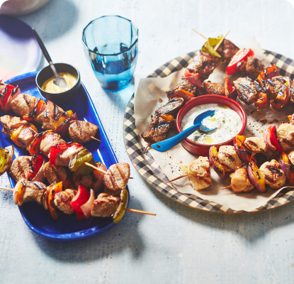 Blue and red plates with chicken, pork and vegetable kabobs hot off the grill