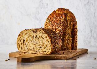 Loaf of Artisan-style Prairie Harvest Multigrain Loaf cut in half, with one section standing cut-side down on wooden cutting board