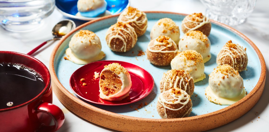 red serving platter of Biscoff Cheesecake truffles with one showing bite taken out, and a hot cup of tea off to the left of the platter.