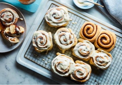Marble surface with cooling rack of glazed cinnamon rolls, with side plate of half-eaten roll to the side
