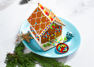 White marble surface with decorated Compliments gingerbread house on blue plate