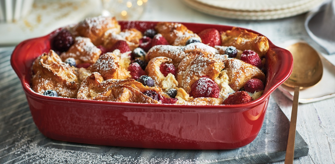 A red casserole dish filled with cooked jumbleberry croissant strata on a set holiday table.