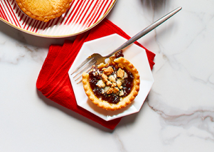 White side plate with mince tart on it next to large red and white striped platter of mixed holiday tarts