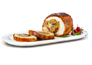 Stuffed, fresh turkey breast filled with pork, cranberry, and apple stuffing on a white serving platter with the first slice carved off.