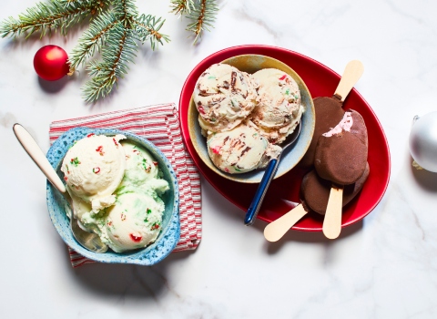 White marble surface with two bowl of ice cream - mistletoe wish and candy cane flavours - and a red side plate with Panache Pink Peppermint & Dark Chocolate Chip Mini Ice Cream Bars
