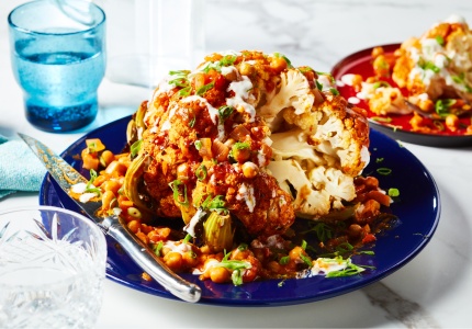 Round blue serving platter of whole-roasted tikka cauliflower with sauce overtop and slice cut out