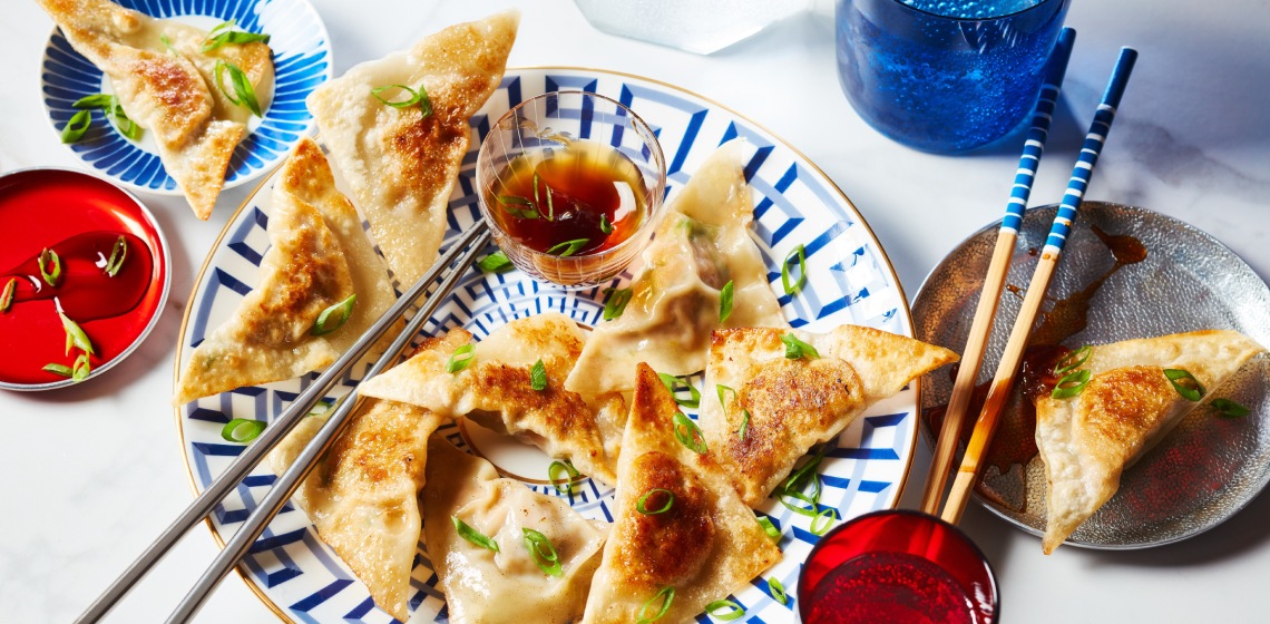 Decorative white and blue plate with gold rim topped with chicken potstickers, chopsticks and small bowl of dipping sauce