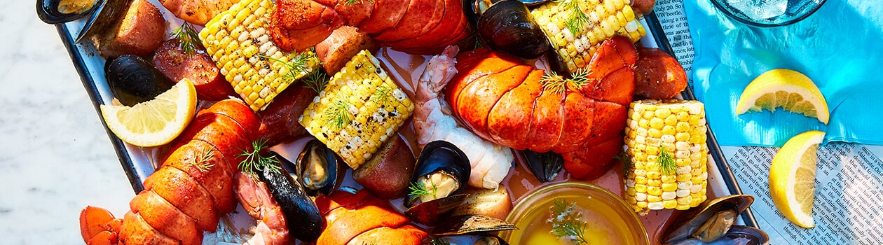 Platter filled with seafood boil with lobster tails, corn, mussels, shrimp, potatoes, and lemon